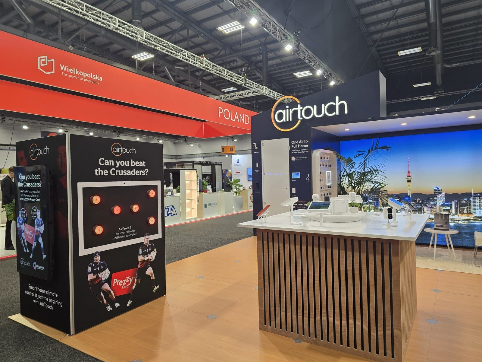 The AirTouch stand at BuildNZ 2026, with the "Can you beat the Crusaders?" interactive wall and the product counter beneath the Auckland skyline backdrop.